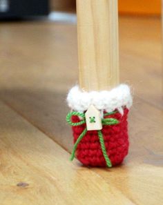 a small red crocheted cup sitting on top of a wooden floor next to a stick