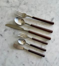 five forks and spoons are lined up on a marble surface