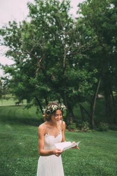 a woman in a white dress holding a piece of paper with flowers on her head