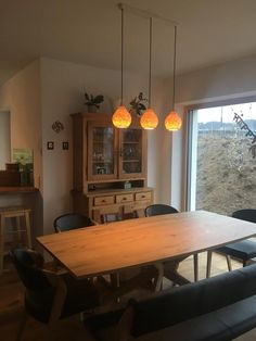 a dining room table with chairs and lights hanging from it's ceiling, next to an open window