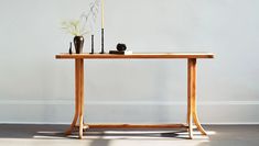 a wooden table with two vases on it and a plant in the middle, against a white wall