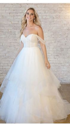 a woman in a white wedding dress standing next to a brick wall