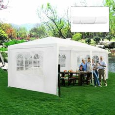 a group of people standing around a white tent on top of a lush green field