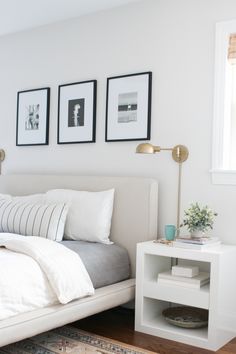 a bedroom with white walls and pictures on the wall above the bed, along with a rug