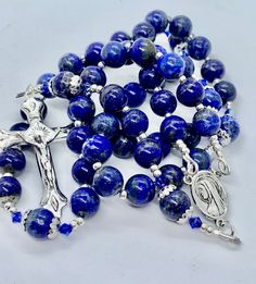 Handmade Catholic Rosary beads made with larger Natural Lapis Lazuli and Capri Swarovski beads.  Perfect as a gift for all occasions .. or for no occasion at all.  This striking Rosary is made using quality materials. Silver 49 strand wire-for added strength and durability, crucifix approximately 5cm x 3.5cm L/W. Silver Miraculous Medal, French wire, silver, silver coated, plated and sterling silver elements. Semi Precious Stone Beads. 10mm Natural Lapis Lazuli Hail Mary beads and Our Father beads.  Rosary length approximately- 51cm Should you acquire this beautiful piece for yourself or as a gift for someone special, you can do so knowing that it was made with love, care and all the reverence due to our beloved Mother Mary. May it bring its bearer peace, love and protection.. today and ev Beads For Men, Rosary Beads Catholic, Catholic Rosary, Swarovski Beads, Hail Mary, Rosary Catholic, Silver Coat, Miraculous Medal, Rosary Beads