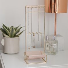 a gold jewelry rack on a white table next to a potted plant