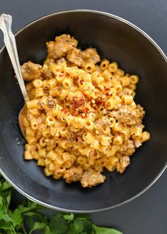 a bowl filled with macaroni and cheese on top of a black table next to some parsley