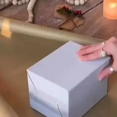 a person's hand reaching into a white box on a table with candles in the background