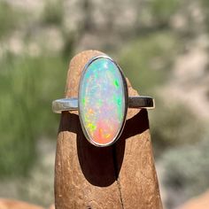 "This opal and silver ring features an oval 16.6 x 8.2 mm, 2.65 carat Ethiopian opal gemstone, set in an artisanal handmade silver bezel ring. We used fine silver for the bezel and American recycled Sterling Silver for the ring band and backplate. This stunning gemstone is milky translucent with confetti-like flashes of blue, green, yellow and red! Ethiopian opal can appear nearly clear or milky without flashes at certain angles or in low light. There are a few tiny pits on one side of the opal Oval Opal Rings With Polished Finish, Polished Opal Ring In Oval Cabochon Shape, Opal Oval Cabochon Ring With Polished Finish, Polished Opal Oval Cabochon Ring, Oval Ethiopian Opal Moonstone Ring, Ethiopian Opal Oval Rings For Anniversary, Classic Ethiopian Opal Ring In Oval Shape, Silver Oval Opal Ring Untreated, Untreated Oval Opal Ring In Silver