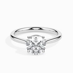 a white gold ring with a round brilliant cut diamond in the center, on a plain surface