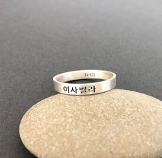 This listing is for a personalized engraved Korean name ring in burnished matte sterling silver. The sample ring is engraved with a name Isabella in Korean in the font #1. Please check the font options in the pictures. Outside and/or inside of the ring can be engraved.  The sample ring is about 3 mm wide.  All orders come gift-wrapped. Avoid dust, moisture and direct light to ensure the jewelry does not tarnish and discolor. << How to order >> Please choose engraving side and ring size from the options. Please leave a name (word, phrase) and font style number you want. We'll translate a name for you if you don't know the language. If you don't choose a font, the font used for the sample will be used and the font #2 will be used for numbers. Meaningful Engraved Silver Stackable Rings, Promise Sterling Silver Engraved Ring, Promise Sterling Silver Ring With Engraved Text, Symbolic Engraved Stackable Rings For Anniversary, Silver Symbolic Jewelry With Engraved Text, Personalized Engraved Ring For Promise, Symbolic Personalized Engraved Promise Ring, Silver Minimalist Ring With Engraved Text, Customizable Minimalist Silver Engraved Ring