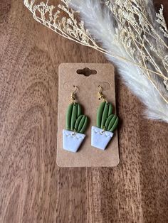 a pair of green and white cactus earrings sitting on top of a wooden table next to dried grass