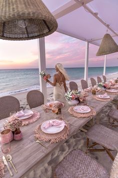 a woman standing on the beach next to a table set with pink plates and napkins