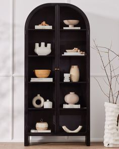 a black bookcase filled with vases and other items on top of a wooden floor