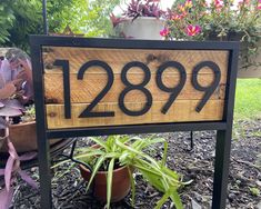 a house number sign sitting on top of a wooden table next to potted plants