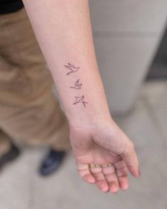 a woman's arm with three small birds tattooed on the left side of her wrist