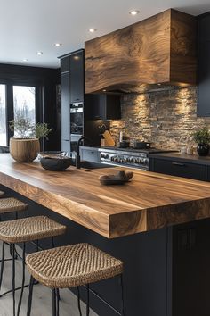 a kitchen with black cabinets and wooden counter tops in front of a stone wall that looks like it has been built into the side of an island