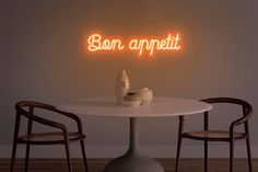 a white table with two chairs and a neon sign above it that says bon appetit