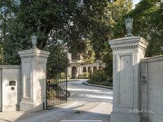 an entrance to a mansion with two statues on either side of the gate and trees in the background