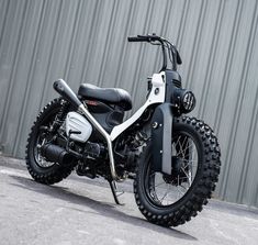 a white and black motorcycle parked in front of a metal building with a wall behind it