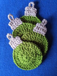 two crocheted green and white ornaments on a blue surface with one ornament in the shape of a christmas tree