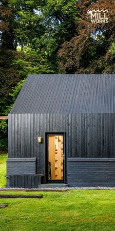 a small black building sitting on top of a lush green field with trees in the background