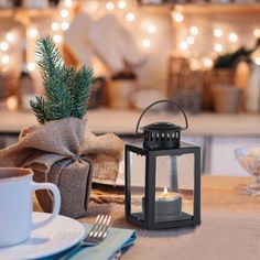 a lit candle sits on a table next to a cup and saucer in front of a christmas tree