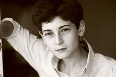 a black and white photo of a young man with his hand on his head, leaning against a wall