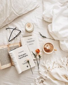 an open book and some flowers on top of a white bed with a cup of coffee