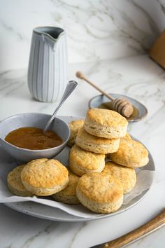 some biscuits are stacked on a plate next to a bowl of peanut butter and honey