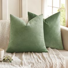 two green pillows sitting on top of a couch next to a cup and saucer