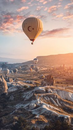 several hot air balloons flying in the sky over some rocks and trees at sunrise or sunset