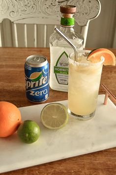 an alcoholic drink on a tray with limes and oranges next to the bottle