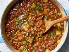 a pot filled with beans and potatoes on top of a counter next to a wooden spoon