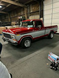 a red and silver truck parked in a garage next to a soda can on the ground