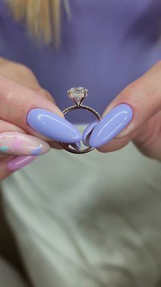 a woman's hands with blue and pink nail polish holding a ring