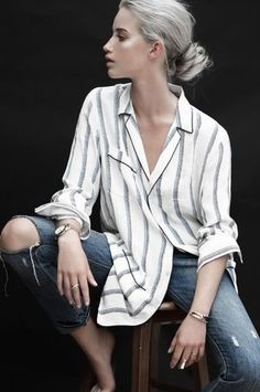 a woman sitting on top of a wooden stool next to a black background wearing jeans and a white shirt