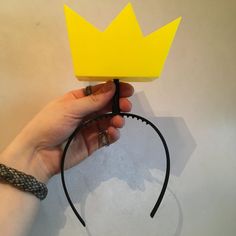 a hand holding a yellow paper crown on top of a headband with black wire