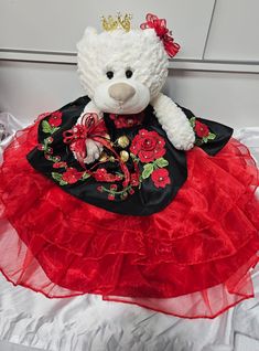 a white teddy bear wearing a red and black dress with roses on it's skirt