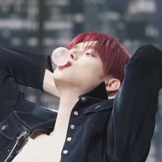 a young man with red hair blowing bubbles into his mouth while wearing a black jacket