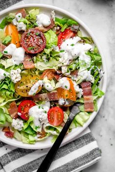 a salad with bacon, tomatoes, lettuce and cheese in a white bowl