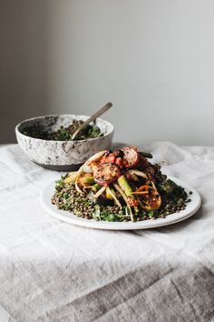 a white plate topped with meat and veggies next to a bowl of lentils