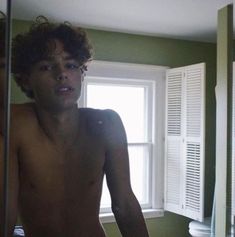 a shirtless young man standing in front of a bathroom mirror