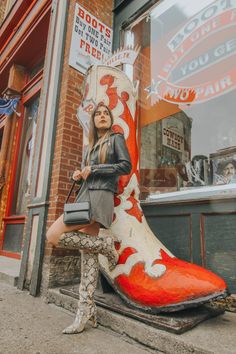 a woman sitting on top of a giant boot in front of a storefront window