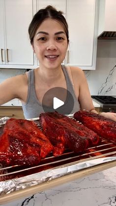 a woman standing in front of an oven with ribs on top of it and another person behind her