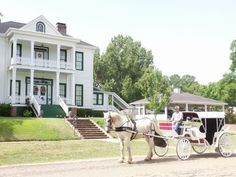 a horse drawn carriage on a road in front of a large white house with stairs