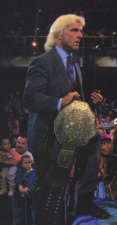 a man in a suit and tie holding a wrestling belt