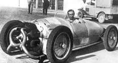 an old black and white photo of a man driving a race car