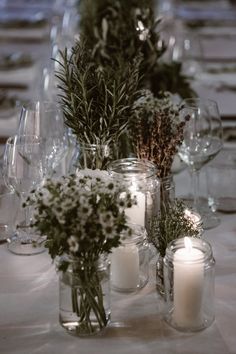 the table is set with candles and vases filled with flowers, herbs and greenery