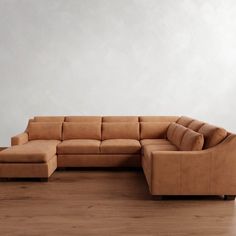 a tan leather sectional sofa sitting on top of a hard wood floor next to a white wall